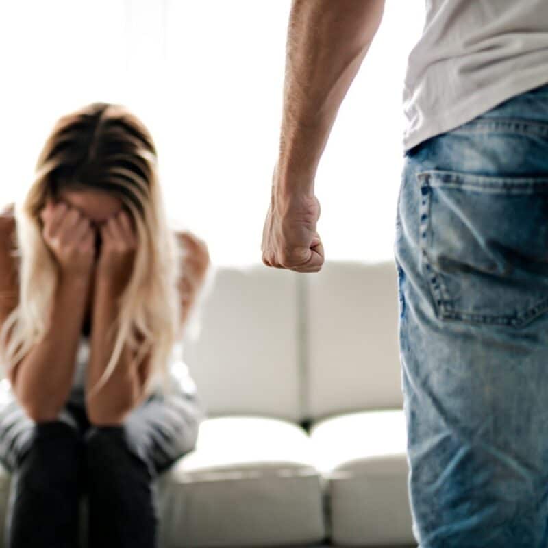 woman sitting on couch with head in hands and man with with clenched fist